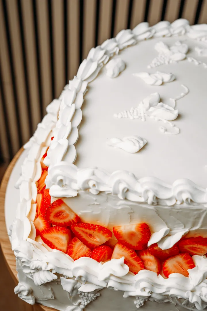 Detalle de conchas de crema de mantequilla hechas a manga y fresas frescas en el borde de una tarta de corazón.