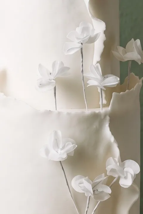 Flores de azúcar blancas con alambre sobre tallos finos, junto a un piso de crema de mantequilla texturizada.