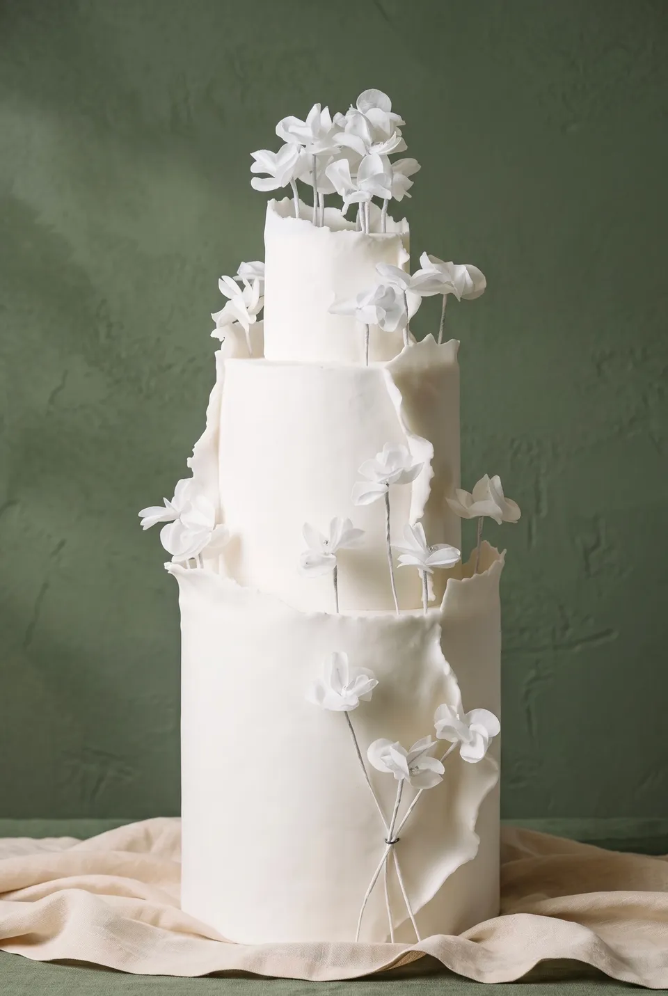 Tarta blanca de tres pisos con altas flores de azúcar con alambre que se alzan entre los pisos.