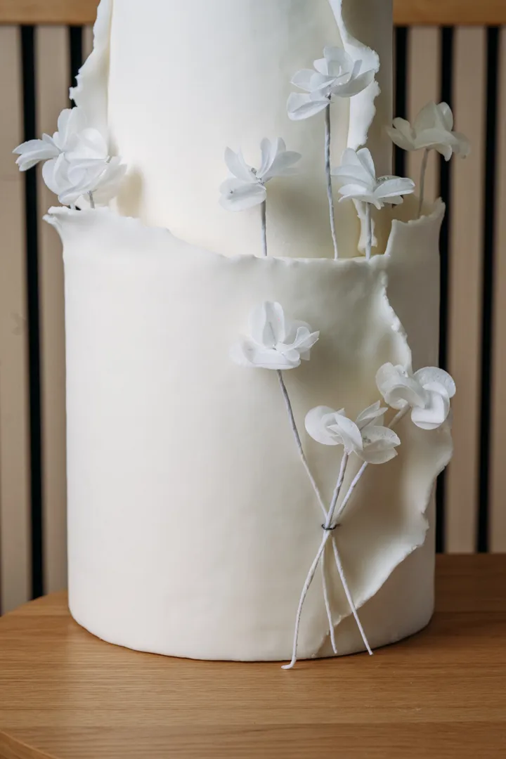 Flores de azúcar blancas con alambre sobre tallos finos, junto a un piso de crema de mantequilla texturizada.