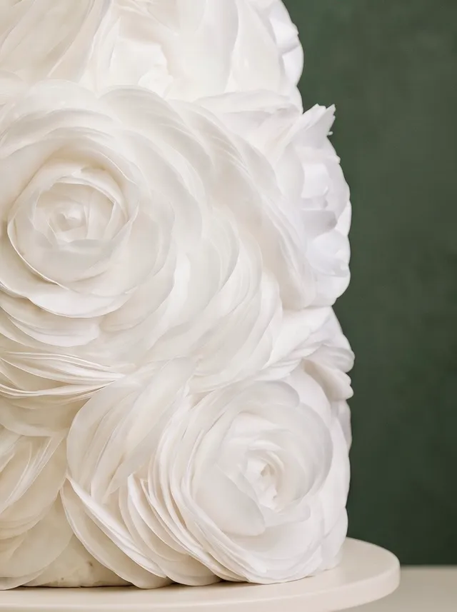 Tarta de dos pisos cubierta por completo de grandes rosas blancas de crema de mantequilla con volantes.